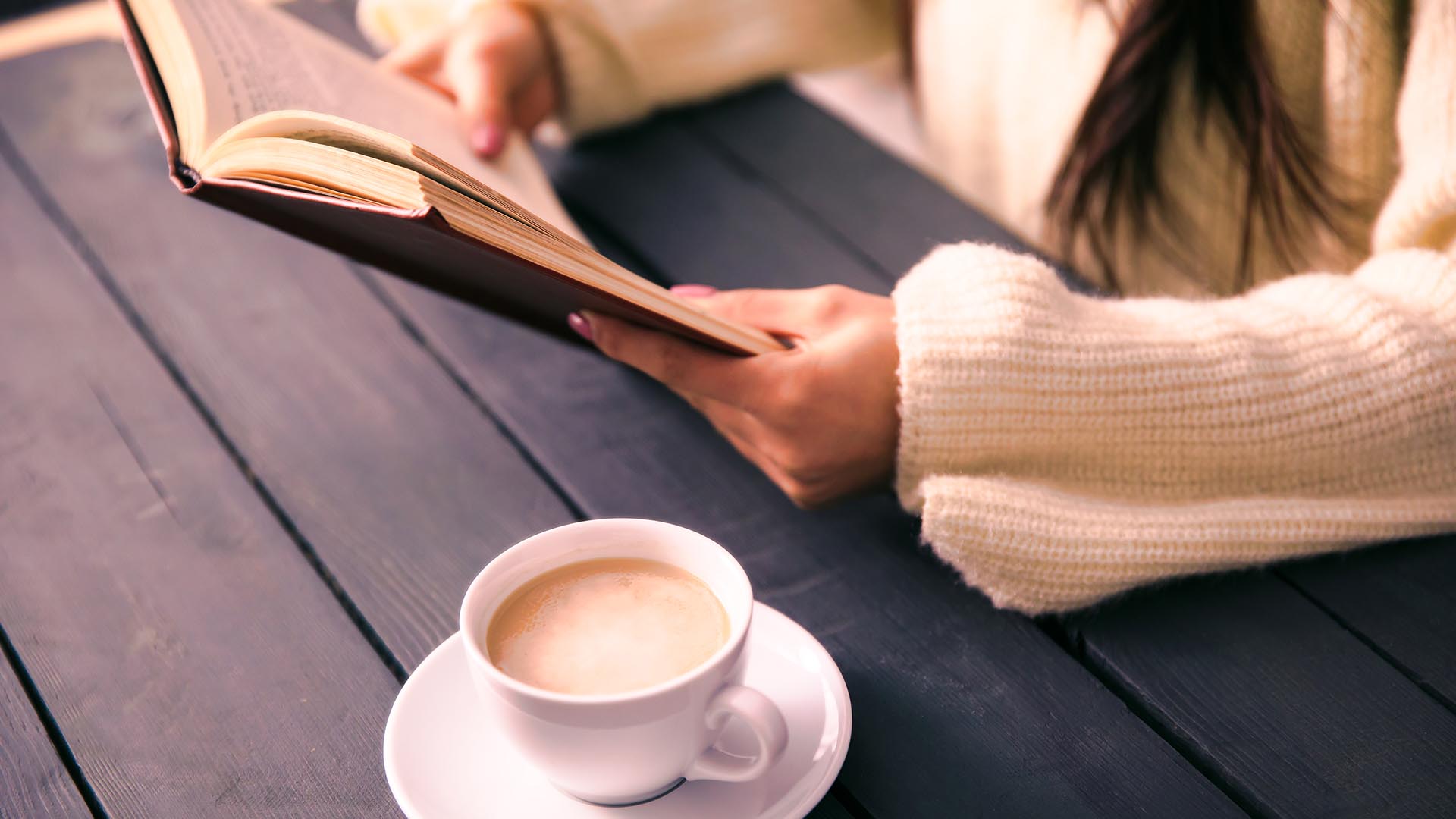Frau lesend am Tisch mit einer Tasse Kaffee